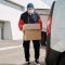 A delivery worker wearing a face mask unloading packages from a van in an urban area.